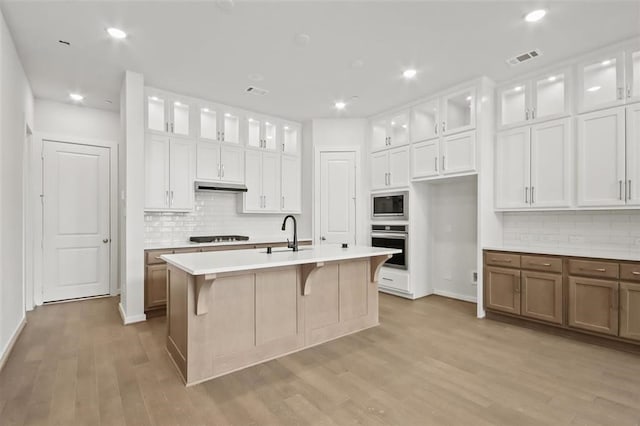 kitchen with oven, under cabinet range hood, light wood-style floors, light countertops, and built in microwave