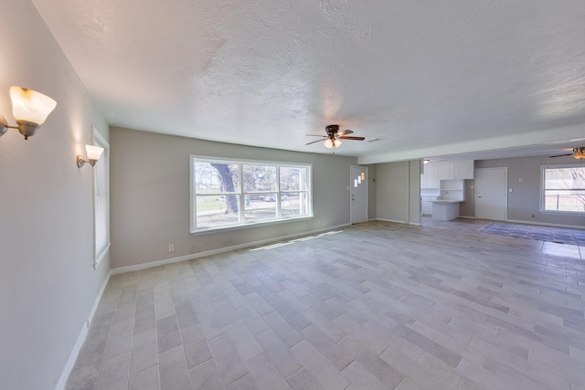 unfurnished living room with a textured ceiling, ceiling fan, light wood-style floors, and baseboards