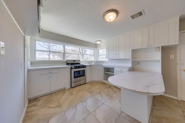 kitchen featuring gas range, a peninsula, white cabinets, and visible vents