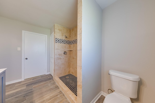 bathroom with toilet, wood finished floors, baseboards, and a stall shower