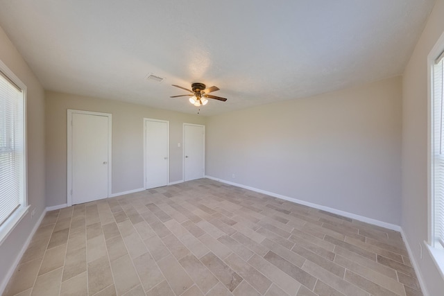 unfurnished bedroom with baseboards, ceiling fan, visible vents, and multiple windows