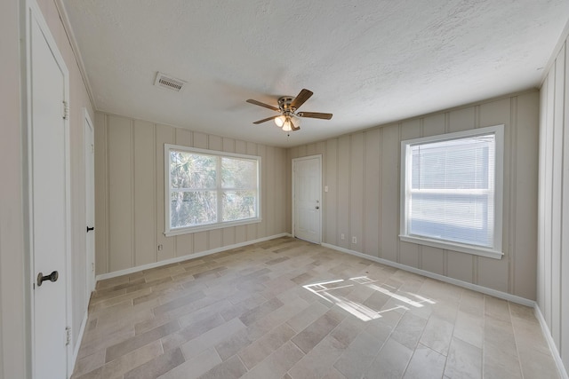 spare room with visible vents, a ceiling fan, baseboards, a textured ceiling, and a decorative wall