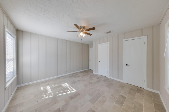 unfurnished bedroom with a textured ceiling, a ceiling fan, visible vents, and a decorative wall