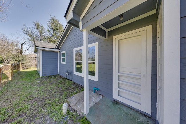 view of exterior entry featuring fence and a yard