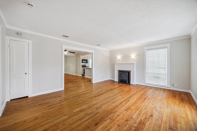 unfurnished living room featuring visible vents, a fireplace with flush hearth, a textured ceiling, crown molding, and light wood-type flooring