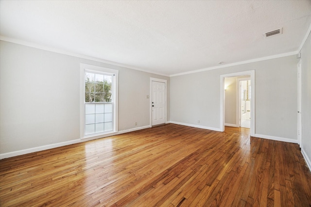 empty room with crown molding, wood finished floors, visible vents, and baseboards