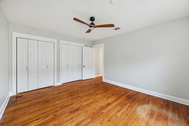 unfurnished bedroom with baseboards, visible vents, two closets, and wood finished floors