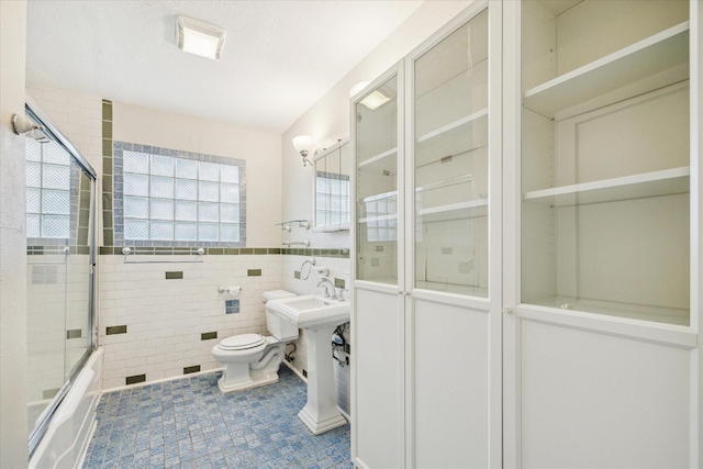 full bathroom with bath / shower combo with glass door, wainscoting, toilet, tile patterned floors, and tile walls