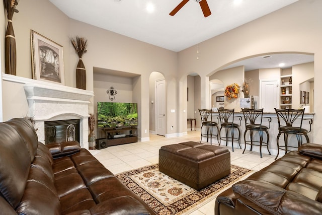 living room with ceiling fan, built in shelves, light tile patterned flooring, and a glass covered fireplace