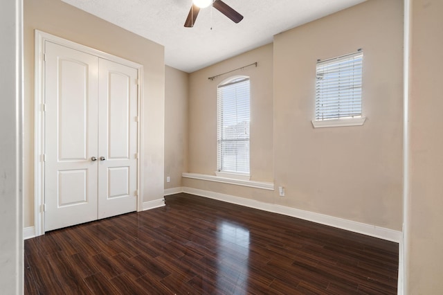 unfurnished bedroom with a textured ceiling, a ceiling fan, baseboards, a closet, and dark wood finished floors