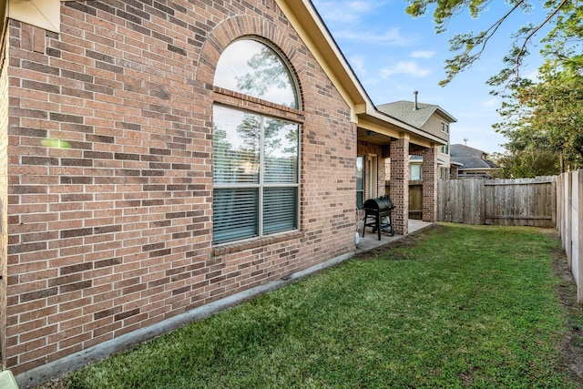 view of side of home with brick siding, a yard, a fenced backyard, and a patio