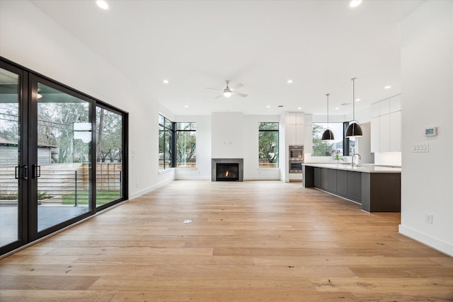 unfurnished living room featuring a sink, a warm lit fireplace, light wood-style floors, and recessed lighting