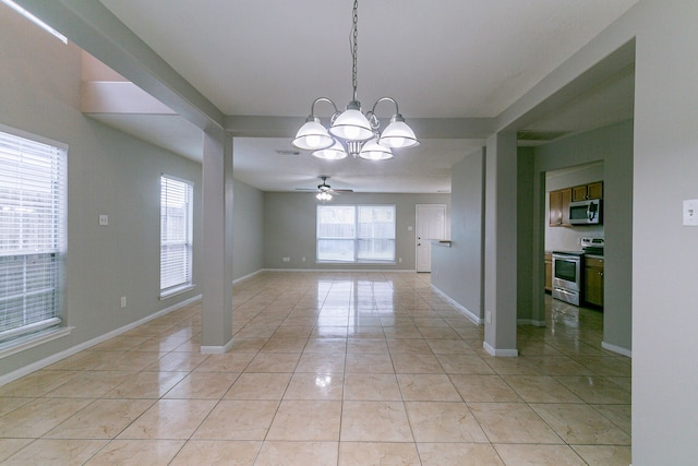 spare room featuring a healthy amount of sunlight, ceiling fan with notable chandelier, baseboards, and light tile patterned flooring