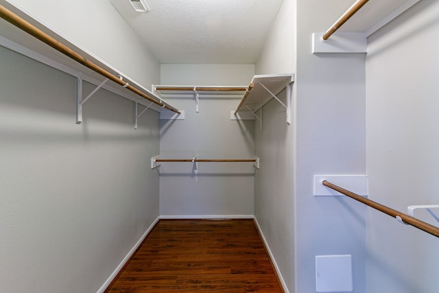 walk in closet with dark wood finished floors