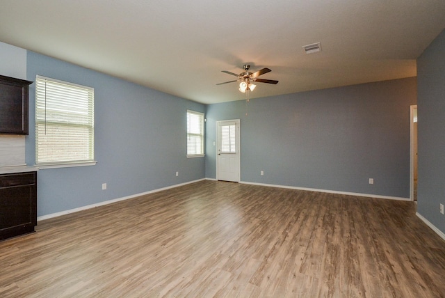 unfurnished room with ceiling fan, wood finished floors, visible vents, and baseboards