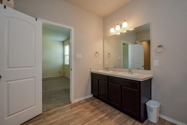 bathroom featuring wood finished floors, a sink, baseboards, and double vanity