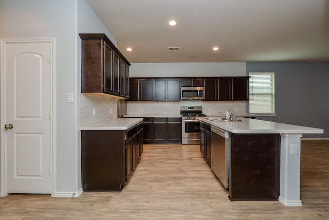 kitchen featuring tasteful backsplash, a center island with sink, light wood-style flooring, stainless steel appliances, and light countertops