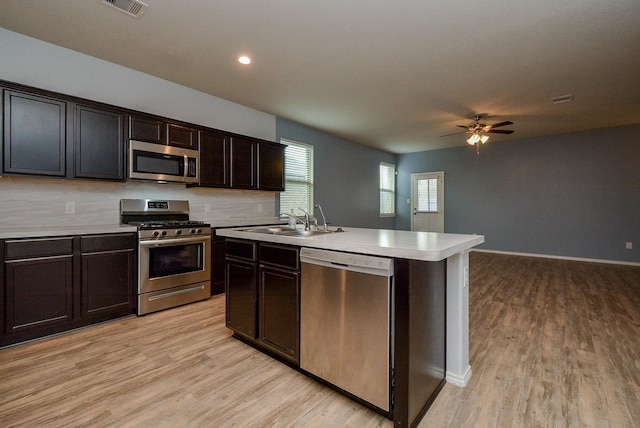 kitchen with light countertops, appliances with stainless steel finishes, a kitchen island with sink, a sink, and dark brown cabinets