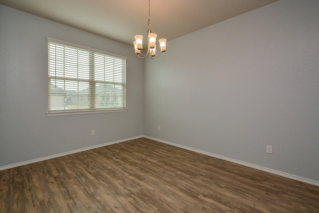 empty room with baseboards, dark wood-type flooring, and a notable chandelier