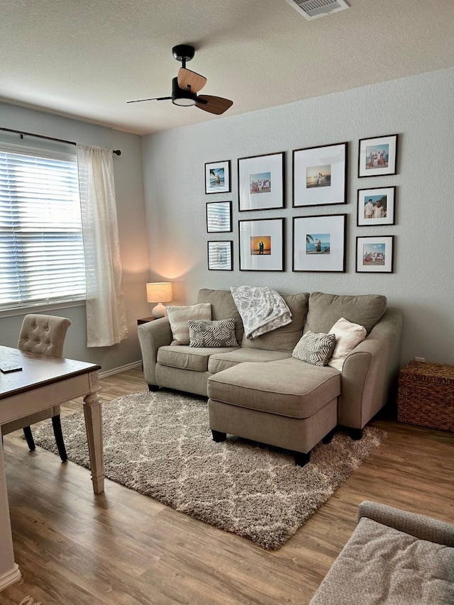 living room with visible vents, a textured ceiling, wood finished floors, and a ceiling fan