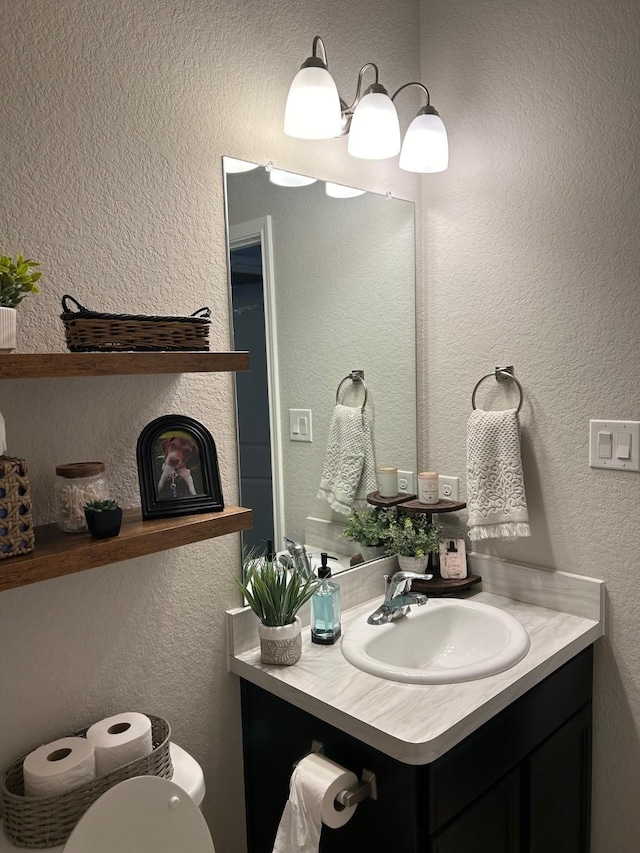 half bath with a textured wall, vanity, and toilet