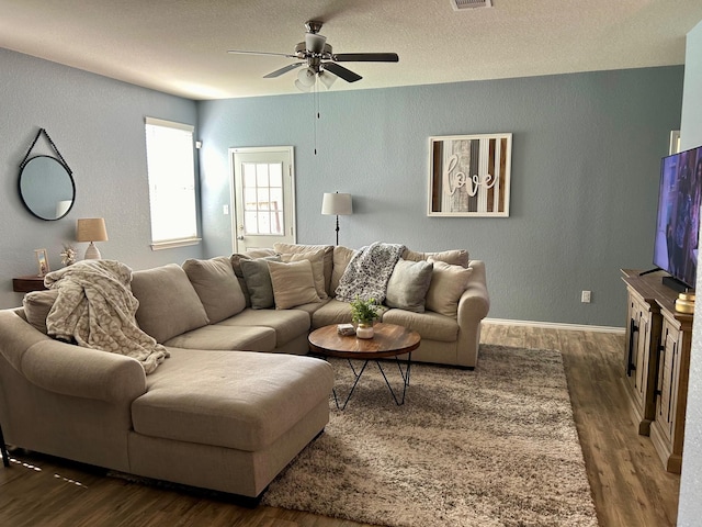 living room featuring dark wood-style floors, a textured wall, ceiling fan, and visible vents