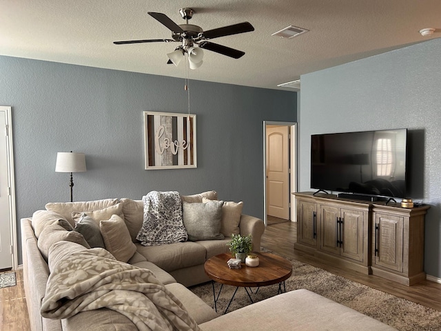 living area with a textured ceiling, ceiling fan, wood finished floors, and visible vents