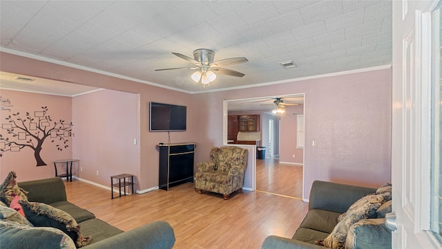 living room with a ceiling fan, visible vents, baseboards, ornamental molding, and light wood finished floors