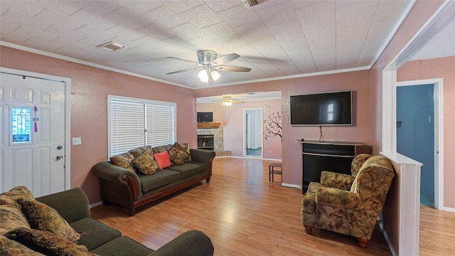 living room with light wood finished floors, baseboards, visible vents, crown molding, and a stone fireplace