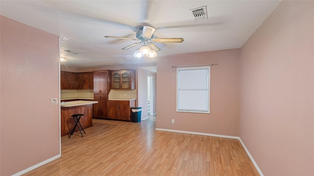 interior space featuring light countertops, visible vents, light wood-style floors, a kitchen breakfast bar, and baseboards