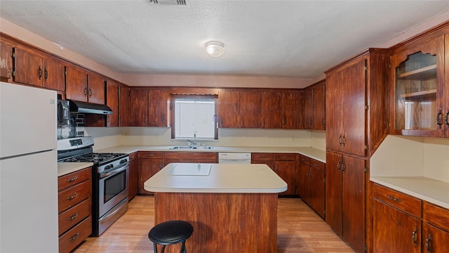 kitchen with white appliances, light wood-style flooring, under cabinet range hood, and a sink