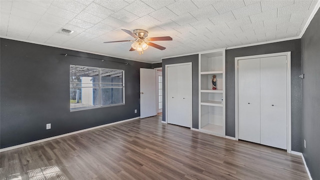 unfurnished bedroom featuring wood finished floors, visible vents, baseboards, multiple closets, and crown molding