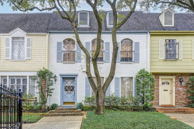 multi unit property featuring brick siding, roof with shingles, and fence