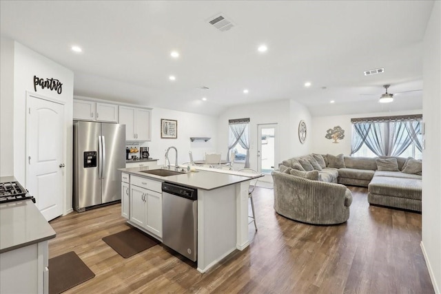 kitchen with stainless steel appliances, open floor plan, an island with sink, white cabinets, and a sink