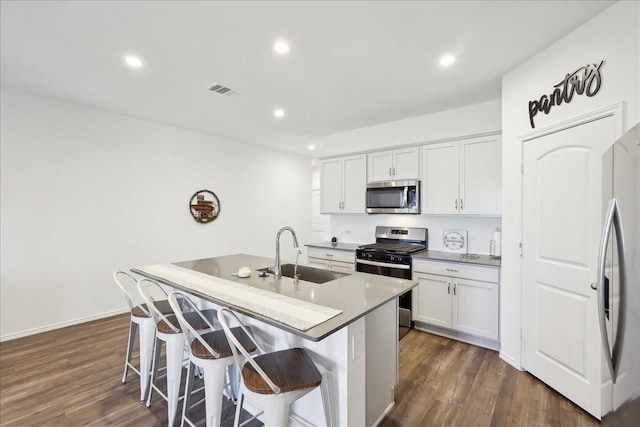 kitchen with a kitchen island with sink, white cabinetry, appliances with stainless steel finishes, and a kitchen bar