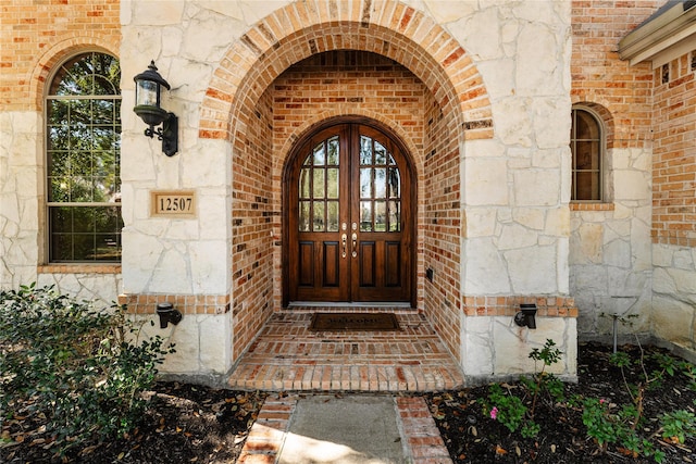 view of exterior entry featuring brick siding, stone siding, and french doors