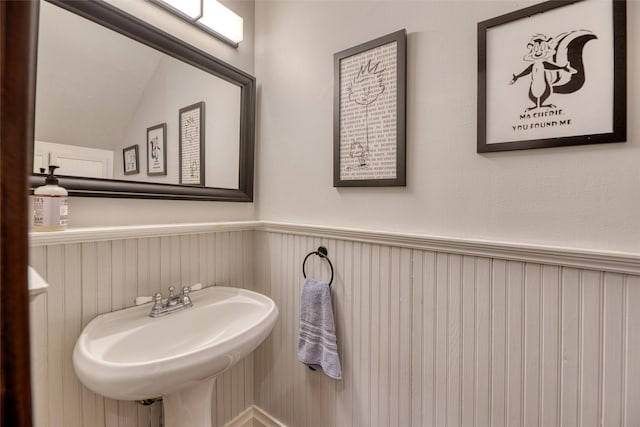 bathroom featuring vaulted ceiling, wainscoting, and a sink