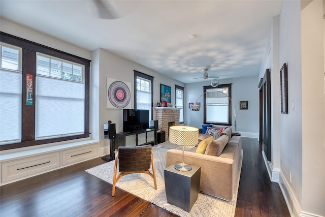 living room featuring dark wood-type flooring, a fireplace, baseboards, and a ceiling fan