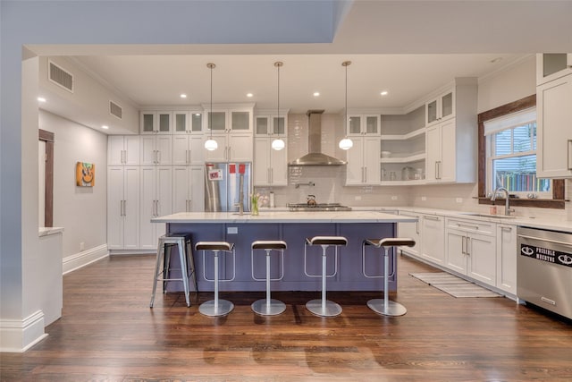 kitchen with stainless steel appliances, light countertops, a kitchen island, and wall chimney range hood