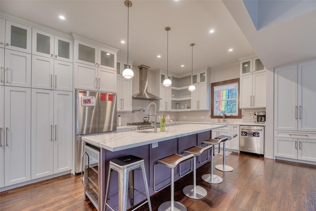 kitchen featuring glass insert cabinets, wall chimney exhaust hood, a kitchen island with sink, and appliances with stainless steel finishes