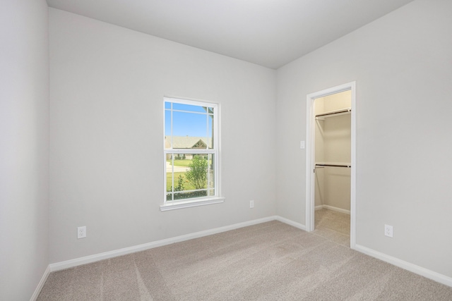 unfurnished bedroom with light carpet, baseboards, a walk in closet, and a closet