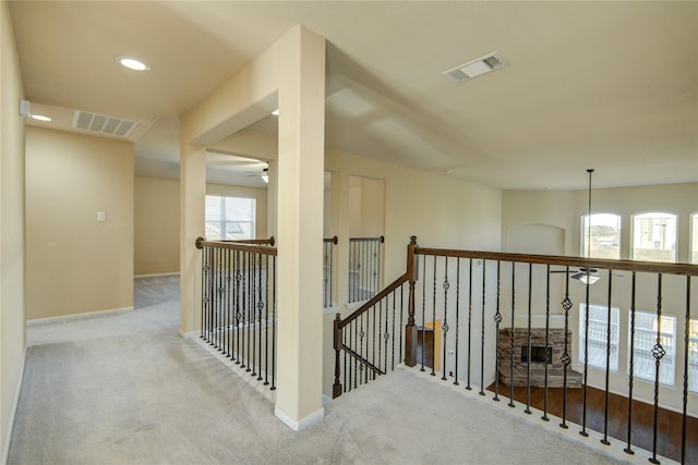 corridor with baseboards, visible vents, light carpet, and an upstairs landing