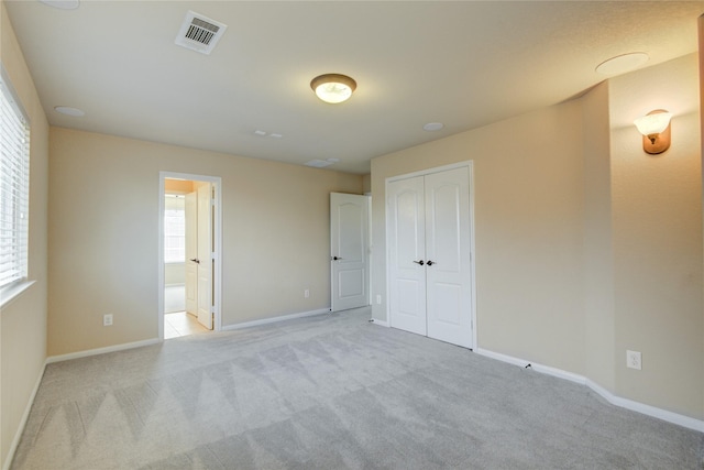 unfurnished bedroom featuring a closet, visible vents, light carpet, connected bathroom, and baseboards