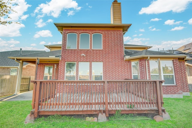 back of house with brick siding, a chimney, a lawn, fence, and a wooden deck