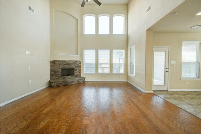 unfurnished living room featuring light wood-style floors, ceiling fan, visible vents, and a stone fireplace