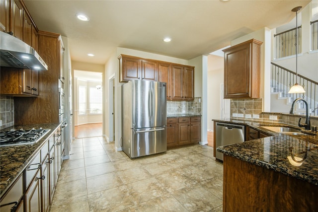 kitchen featuring a sink, appliances with stainless steel finishes, range hood, dark stone countertops, and pendant lighting