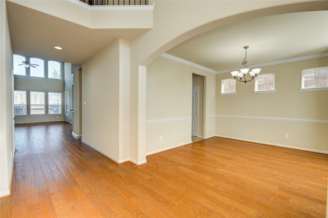 unfurnished room featuring arched walkways, crown molding, wood finished floors, baseboards, and ceiling fan with notable chandelier