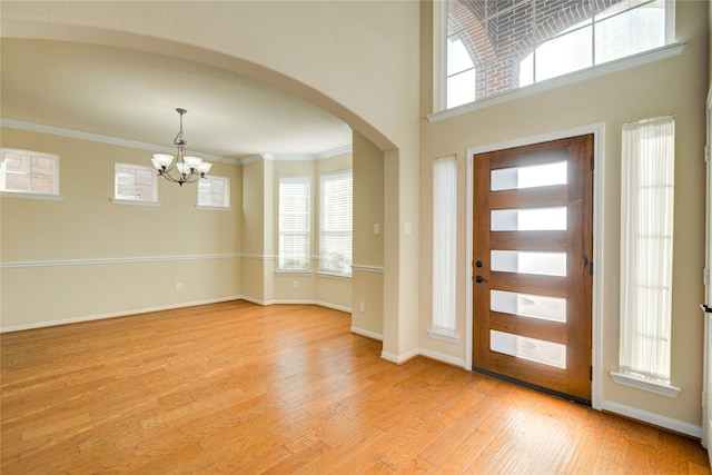 foyer entrance featuring arched walkways, light wood-style flooring, a towering ceiling, baseboards, and crown molding