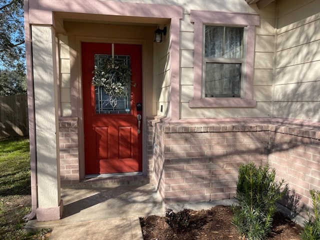 doorway to property with brick siding and fence