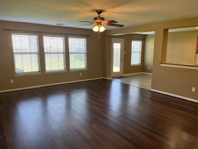 empty room with dark wood-style floors, a ceiling fan, and baseboards